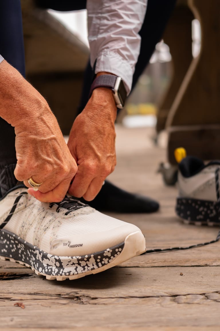 Hände schnüren einen weißen Joe Nimble Trail-Schuh, der zweite Schuh steht daneben